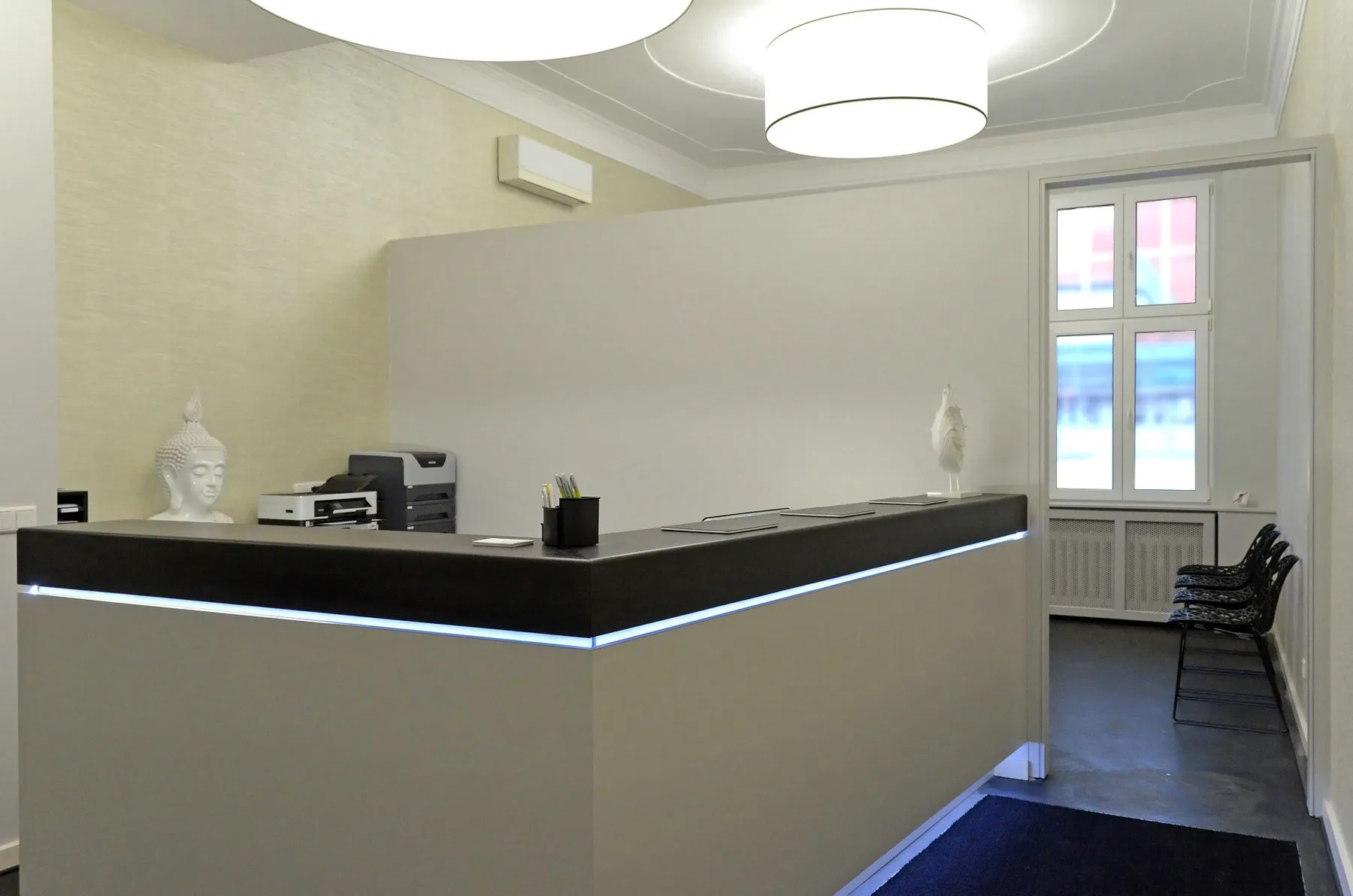 Empfang der Privatpraxis Blasenzentrum Westend: dunkler Tresen mit Lichtband, Buddha-Köpfe, Altbau